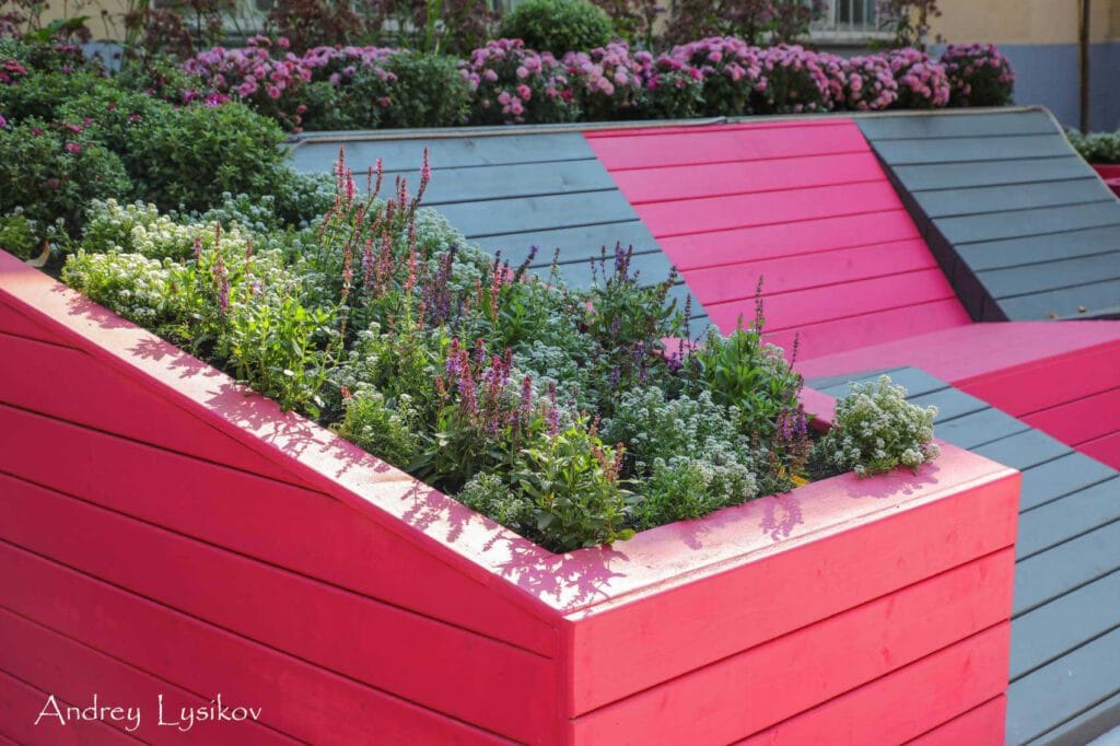 Istutuslaatikko kukilla. Kuvassa on punainen ja vaaleanpunainen väri. Mukana myös ulkona, rakennus, huonekasvi.