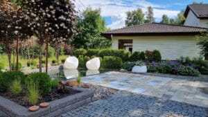 Piha, jossa on suihkulähde ja kukkia. Kuvassa on harmaa ja musta väri. Huoneessa on myös ulkona, taivas, maisemointi.