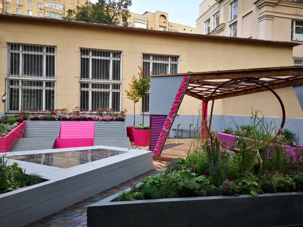 Värikäs puutarha rakennuksen edessä. Kuvassa on harmaa ja musta väri. Huoneessa on myös ulkona, ikkuna, taivas.