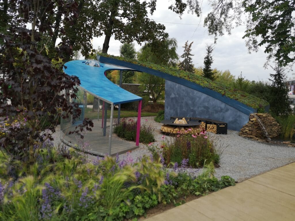 Pieni sininen teltta puutarhassa. Kuvassa on harmaa ja musta väri. Mukana myös ulkona, kasvi, puu.