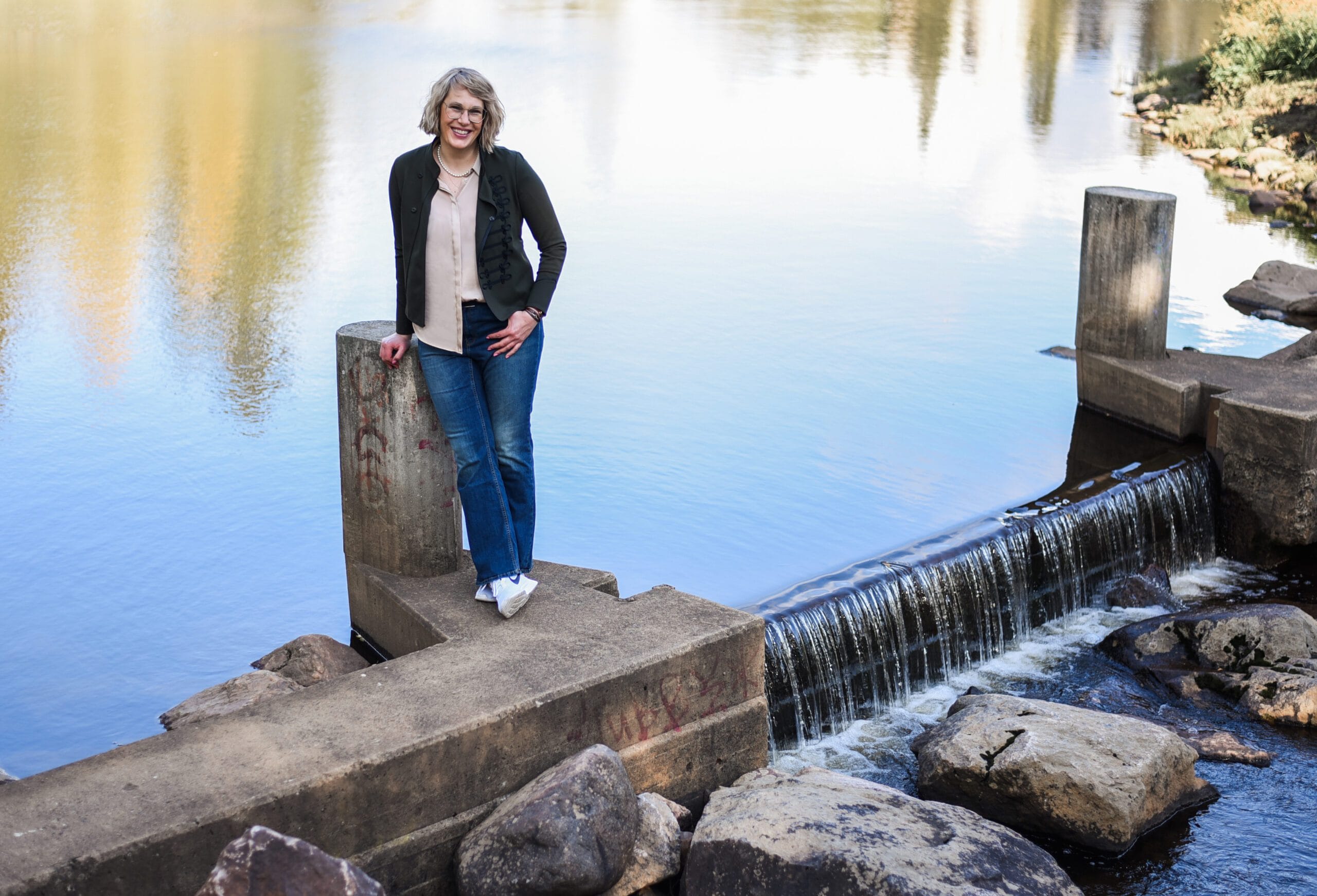 Mies seisoo kivellä vesistön edessä. Kuvassa on valkoinen ja harmaa väri. Näyttää yhden henkilön. Sisältää myös vaatteita, ulkoilua, farkkuja.