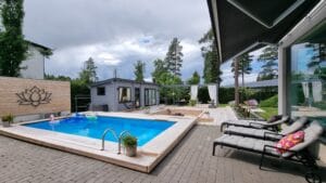 Uima-allas, jossa on kansi ja tuoleja. Kuvassa on harmaat ja mustavalkoiset värit. Sisältää kasvin, penkin ja uima-altaan. Mukana myös rakennus, taivas, puu.