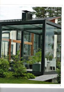 Lasitalo, jossa on suuri lasinen etupiha. Kuvassa on valkoinen ja harmaa sekä musta värit. Huoneessa on myös ulkona, ikkuna, huonekasvi.