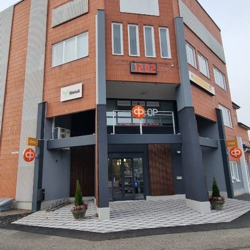 Rakennus, jonka edessä on kyltti. Kuvassa on harmaa ja valkoinen väri. Huoneessa on myös ulkona, taivas, ikkuna.