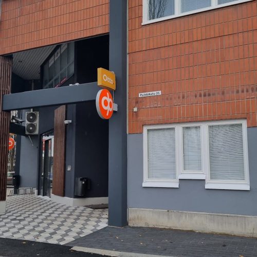 Rakennus, jonka edessä on kyltti. Kuvassa on harmaa ja ruskea väri. Huoneessa on myös ulkona, taivas, auto.