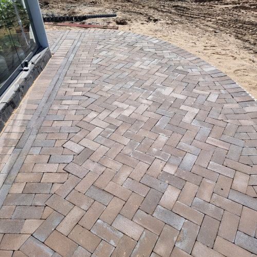 Tiilinen kävelytie, jossa on aita. Kuvassa on harmaat värit. Mukana myös maa-, ulko-, paasikivi.