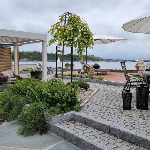 Patio, jossa on pöytä ja tuolit ja sateenvarjot. Kuvassa on harmaa ja valkoinen väri. Sisältää tuolin ja sateenvarjon. Huoneessa on myös ulkona, taivas, huonekalut.