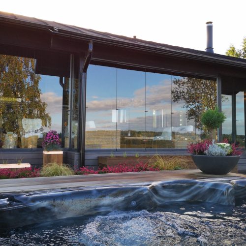 Rakennus, jossa on lasinen etuosa. Kuvassa on harmaa ja valkoinen sekä musta väri. Mukana myös taivas, ulkona, kasvi.