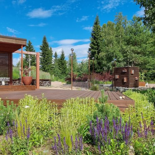 Henkilö, joka istuu penkillä puutarhassa. Kuvassa on vihreitä värejä. Mukana myös ulkona, taivas, pilvi.