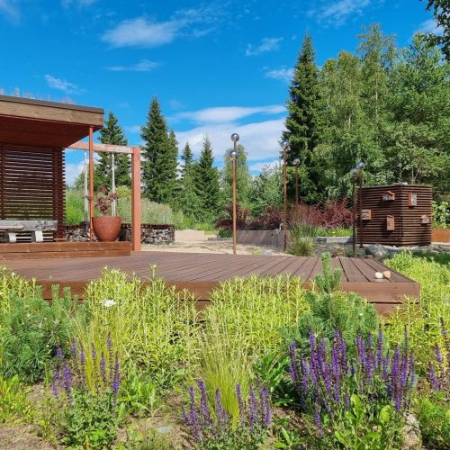 Henkilö, joka istuu penkillä puutarhassa. Kuvassa on vihreitä värejä. Mukana myös ulkona, taivas, pilvi.