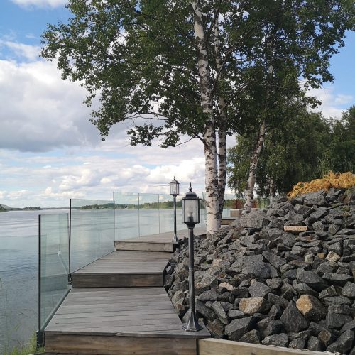 Puinen laituri, jossa on lyhtypylväs ja puu vesistön vieressä. Kuvassa on harmaa ja valkoinen väri. Sisältää myös ulkona, pilvi, järvi.