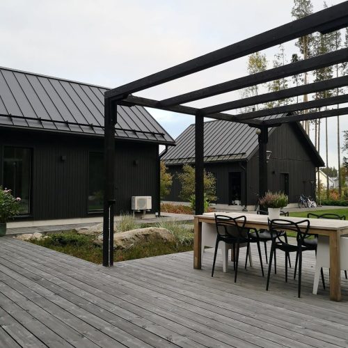 Puinen kansi, jossa on pöydät ja tuolit. Kuvassa on harmaa ja valkoinen sekä musta väri. Huoneessa on myös ulkona, taivas, huonekalut.