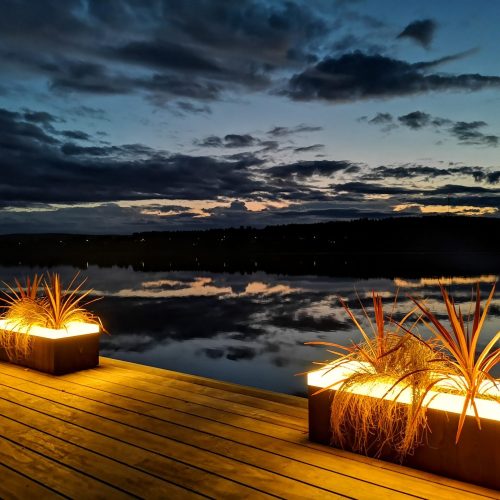 Kansi, jolla on ryhmä valaistuja ruukkukasveja. Kuvassa on mustan ja ruskean värit. Mukana myös pilvi, ulkona, taivas.