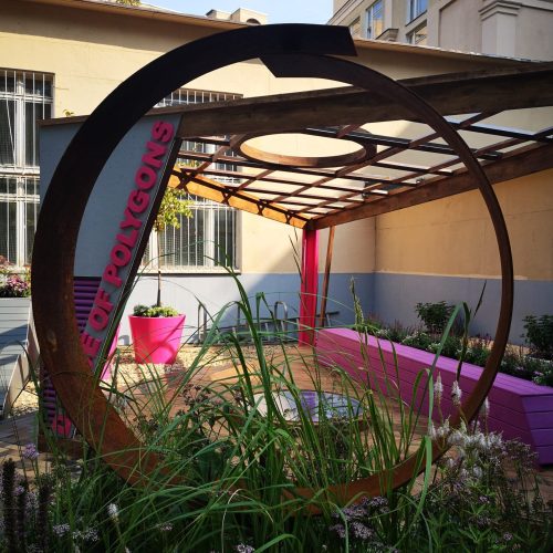 Värikäs kyltti rakennuksen edessä. Kuvassa on mustan ja harmaan värit. Huoneessa on myös ulkona, taivas, ikkuna.