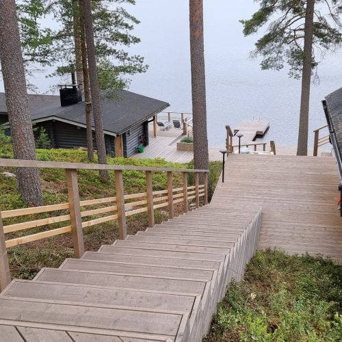 Puinen kansi, jonka taustalla on talo ja puita. Kuvassa on harmaat värit. Sisältää myös ulkona, kasvina, rakennuksena.