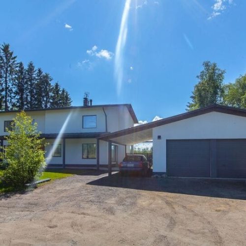 Talo, jossa on autotalli ja puita. Kuvassa on sininen ja harmaa väri. Sisältää Vanin ja puun. Mukana myös ulko-, taivas-, maa-ajoneuvo.