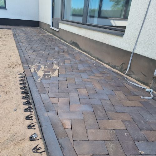 Tiilinen kävelytie rakennuksen vieressä. Kuvassa on harmaat värit. Sisältää myös maadoitettua, ulkona, komposiittimateriaalia.