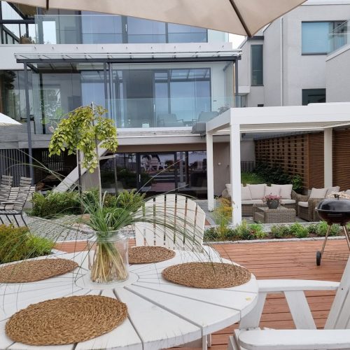 Patio, jossa on pöytiä ja tuoleja. Kuvassa on harmaa ja valkoinen sekä ruskea väri. Sisältää sateenvarjon ja tuolin. Mukana myös ulkona, kasvi, huonekasvi.