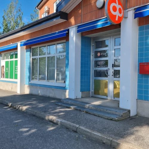 Rakennus, jonka edessä on kyltti. Kuvassa on harmaat värit. Huoneessa on myös ulkona, ikkuna, taivas.