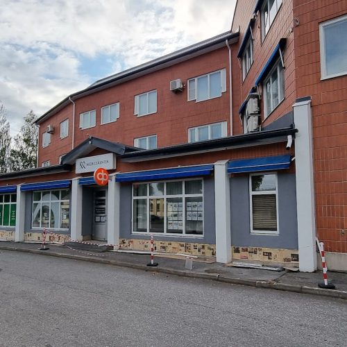 Rakennus, jonka edessä on kyltti. Kuvassa on harmaa ja ruskea ja valkoinen. Mukana myös ulkona, taivas, pilvi.