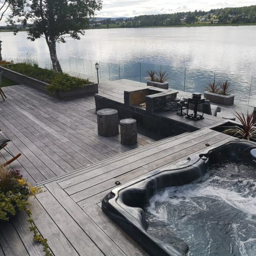 Kansi, jossa on pöytiä ja tuoleja vesistön vieressä. Kuvassa on harmaa ja valkoinen sekä musta väri. Mukana myös ulkona, puu, kasvi.