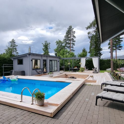 Uima-allas, jossa on kansi ja tuoleja. Kuvassa on harmaat ja mustavalkoiset värit. Sisältää kasvin, penkin ja uima-altaan. Mukana myös rakennus, taivas, puu.