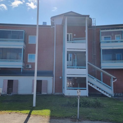 Punainen auto pysäköitynä rakennuksen eteen. Sisältää ikkunan ja auton. Mukana myös ulko-, taivas-, maa-ajoneuvo.