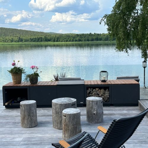 Laituri, jonka taustalla on vesistö ja puita. Kuvassa on valkoinen ja harmaa sekä musta värit. Sisältää ruukkukasveja ja -kasveja. Mukana myös ulkona, taivas, pilvi.