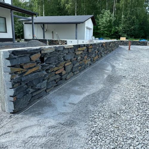 Kivimuuri, jossa on kiviseinä. Kuvassa on harmaat värit. Sisältää myös ulkona, maassa, rakennuksessa.