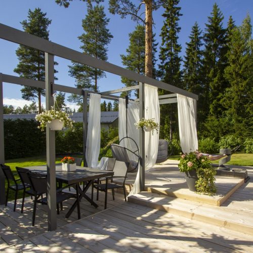 Patio, jossa on pöytä ja tuolit. Kuvassa on harmaa ja musta väri. Sisältää tuolin, kasvin ja ruokapöydän. Mukana myös ulkona, puu, taivas.