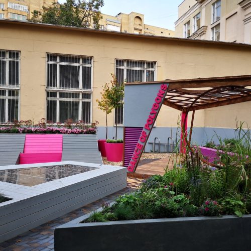 Värikäs puutarha rakennuksen edessä. Kuvassa on harmaa ja musta väri. Huoneessa on myös ulkona, ikkuna, taivas.