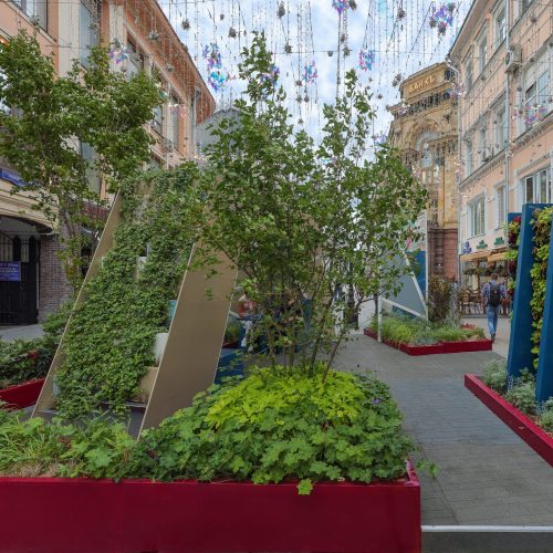 Katu, jossa on rakennuksia ja kasveja. Kuvassa on harmaa ja vihreä väri. Huoneessa on myös ulkona, ikkuna, kukkaruukku.