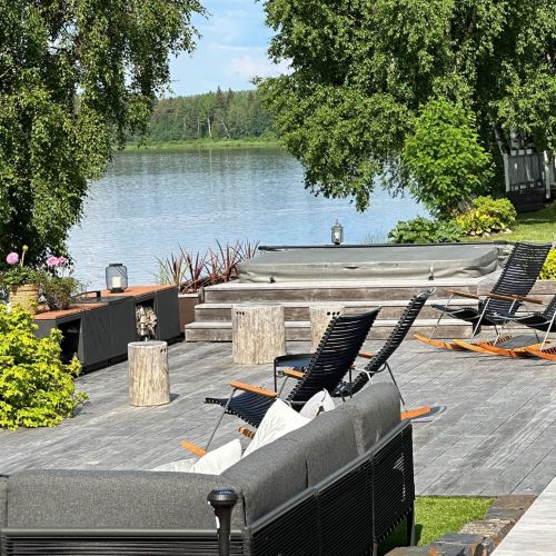 Patio, jossa on tuoleja ja pöytä vesistön vieressä. Kuvassa on harmaa ja vihreä ja valkoinen väri. Huoneessa on myös ulkona, puu, penkki.