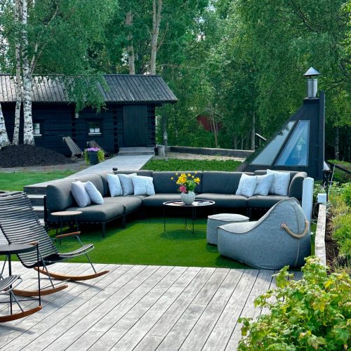 Patio, jossa on pöytä ja tuolit sekä takka. Kuvassa on vihreän ja valkoisen sekä harmaan värit. Sisältää sohvan, tuolin, istuimet ja kasvin. Huoneessa on myös ulkoilu, puu, maisemointi.