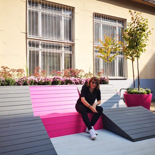 Henkilö, joka istuu portaikossa. Kuvassa on harmaa ja valkoinen väri. Sisältää kasvin, jalkineet ja henkilön. Näyttää yhden henkilön. Huoneessa on myös rakennus, vaatteet, ulkona.