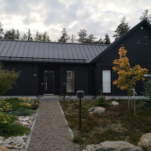 Talo, jossa on sora-ajotie. Kuvassa on mustaharmaa ja valkoinen väri. Sisältää kasvin, puun ja talon. Sisältää myös ulkona, pilvenä, rakennuksena.