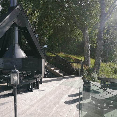 Puinen kansi, jossa on lyhty ja puita sekä vesistö. Kuvassa on harmaa ja valkoinen sekä musta väri. Sisältää myös ulkona, kasveja, huonekaluja.