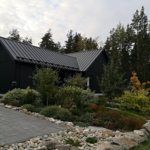 Talo, jossa on kivipolku. Kuvassa on valkoinen ja harmaa sekä musta värit. Sisältää myös ulkona, pilvenä, kasvina.