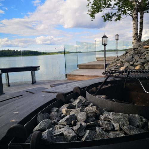 Laituri, jonka taustalla on kiviä ja vesistö. Kuvassa on mustaharmaa ja valkoinen väri. Mukana myös ulkona, pilvi, taivas.