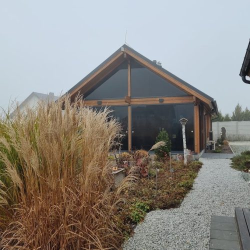 Rakennus, jonka edessä on puutarha. Kuvassa on valkoinen ja harmaa sekä ruskea väri. Mukana myös ulkona, kasvi, taivas.