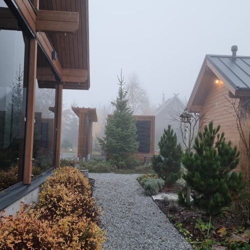 Polku rakennusten välillä. Kuvassa on valkoinen ja harmaa sekä ruskea väri. Mukana myös ulkona, taivas, puu.