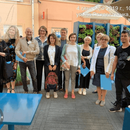 Ryhmä ihmisiä poseeraa valokuvassa. Kuvassa on harmaa ja musta väri. Sisältää käsilaukun ja henkilön. Sisältää myös vaatteita, jalkineita, naisen.