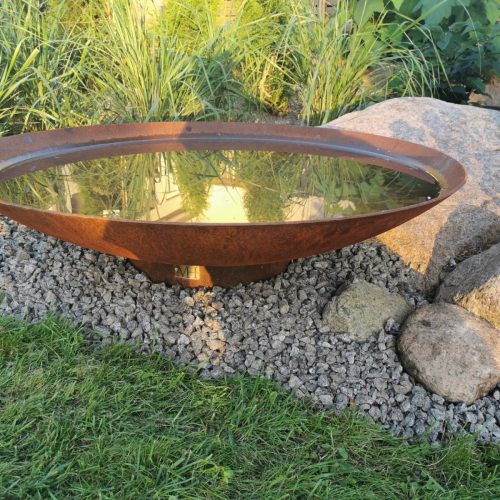 Pyöreä metallinen pesuallas kalliolla. Kuvassa on harmaa ja vihreä väri. Huoneessa on myös ulkona, ruoho, puutarha.