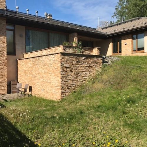 Tiilirakennus, jonka edessä on penkki. Kuvassa on mustia värejä. Sisältää myös ulkona, ruohoa, kasveja.