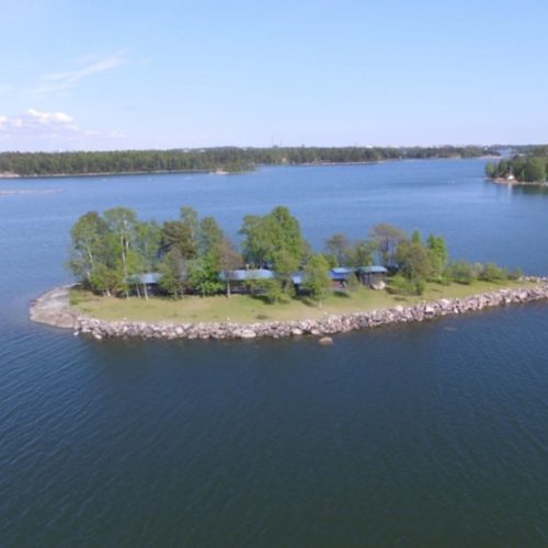 Saari, jossa on puita ja taloja. Huoneessa on myös ulkona, vettä, taivas.