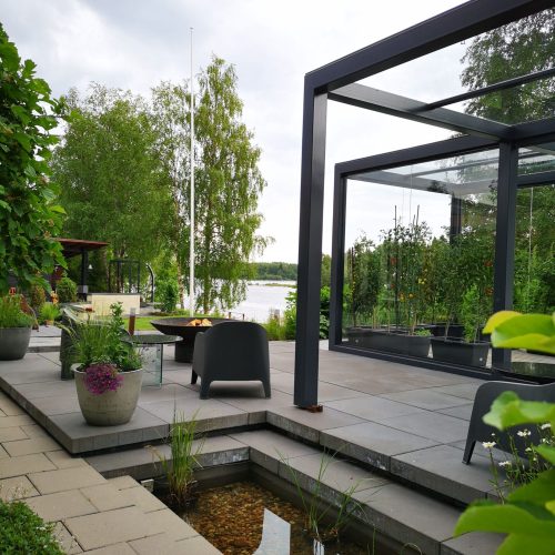 Patio, jossa on pöytä ja tuolit. Kuvassa on valkoinen ja harmaa sekä vihreä väri. Sisältää kasvi- ja ruukkukasveja. Mukana myös taivas, ulkona, kukkaruukku.