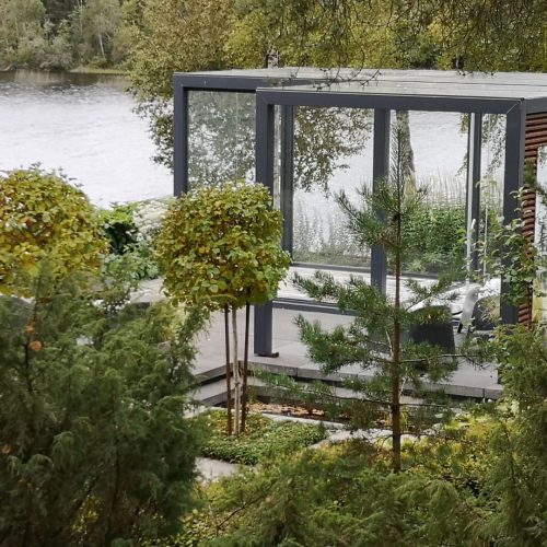 Talo, jossa on lasiseinä. Kuvassa on harmaa ja valkoinen väri. Mukana myös puu, ulkona, kasvi.