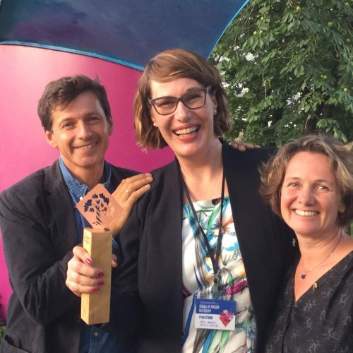 Ryhmä ihmisiä poseeraa valokuvassa. Kuvassa on mustia värejä. Sisältää aurinkolasit, puun ja henkilön. Näyttää 3 henkilöä. Sisältää myös ihmisen kasvot, vaatteet, ulkona.