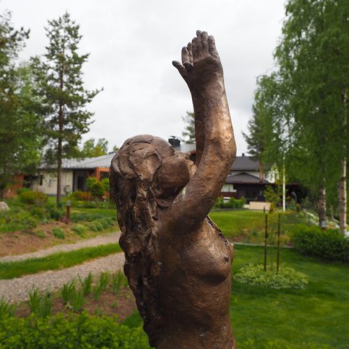 Kanto, jonka taustalla on talo. Kuvassa on vihreä ja valkoinen väri. Sisältää puun ja veistoksen. Sisältää myös ulkona, ruohoa, kasveja.