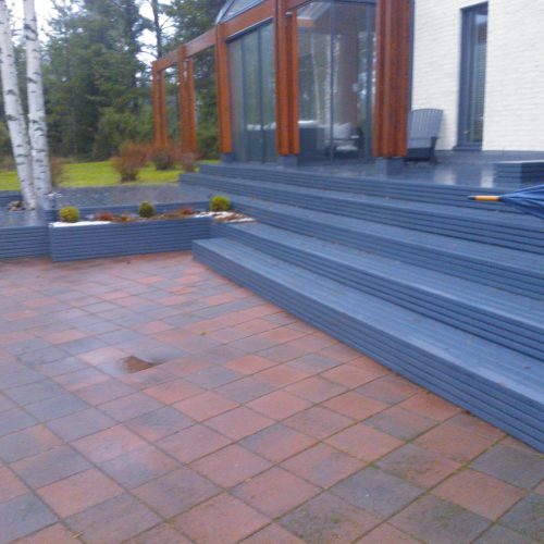 Penkki rakennuksen edessä. Kuvassa on harmaat värit. Huoneessa on myös ulkona, puu, portaat.